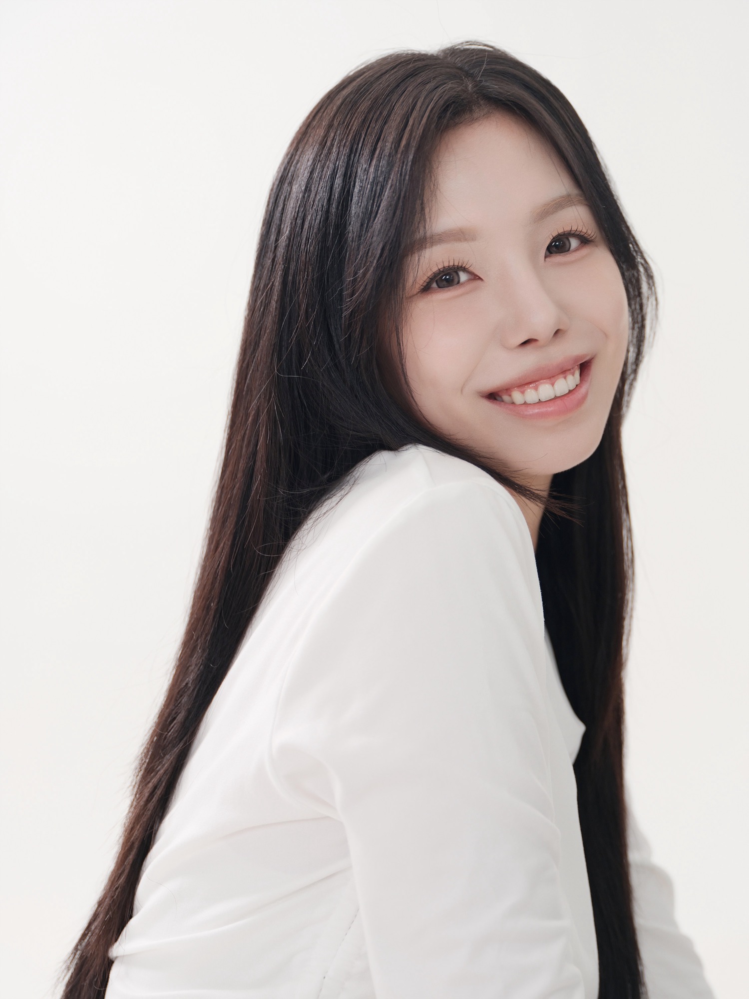 밝은 배경에서 흰 블라우스를 입고 어깨 너머로 웃는 긴 생머리 여성 배우 프로필