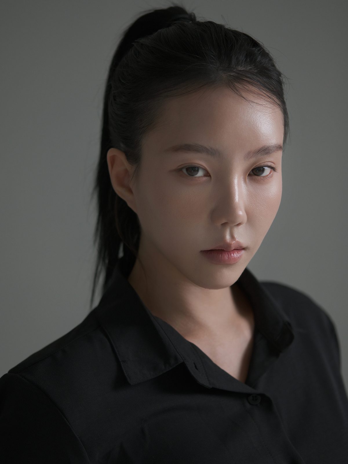 검은 셔츠를 입고 머리를 묶은 여성 배우의 어두운 톤 클로즈업