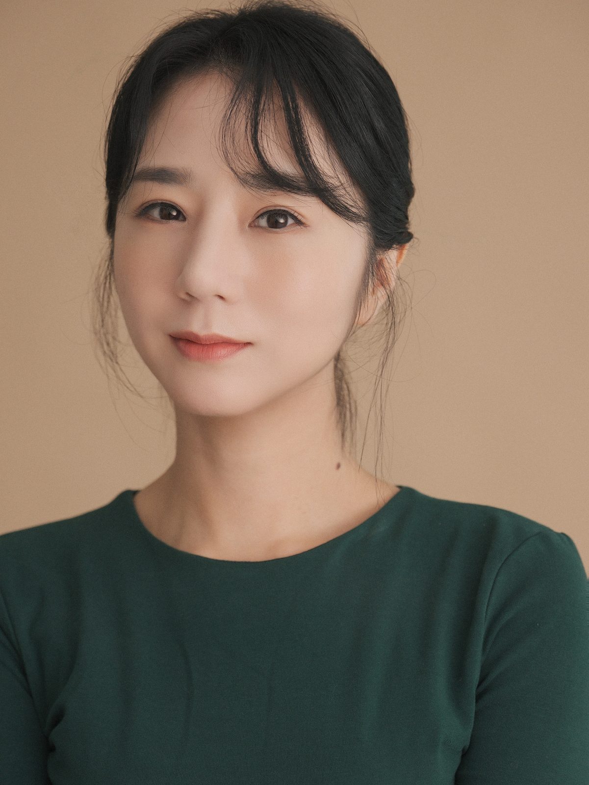 베이지 배경에서 초록 상의를 입은 여성 배우 클로즈업