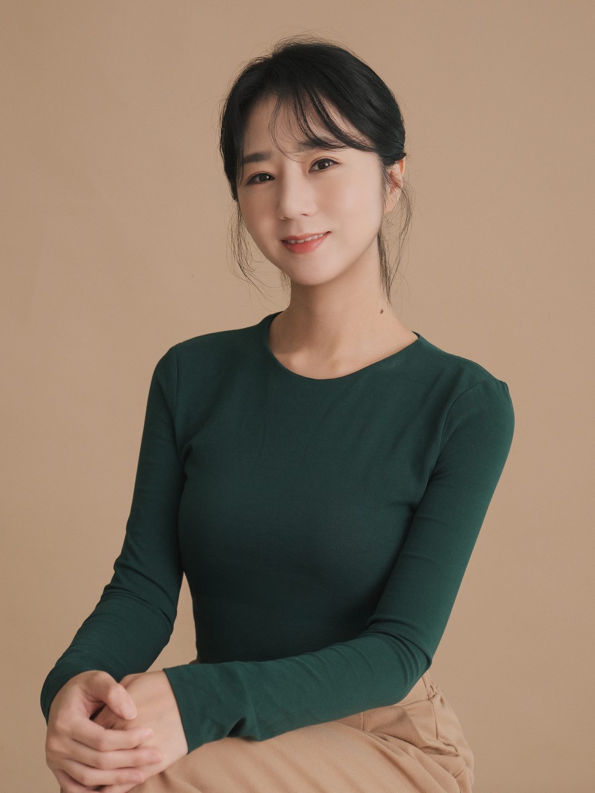 베이지 배경에서 초록 상의를 입고 앉은 여성 배우