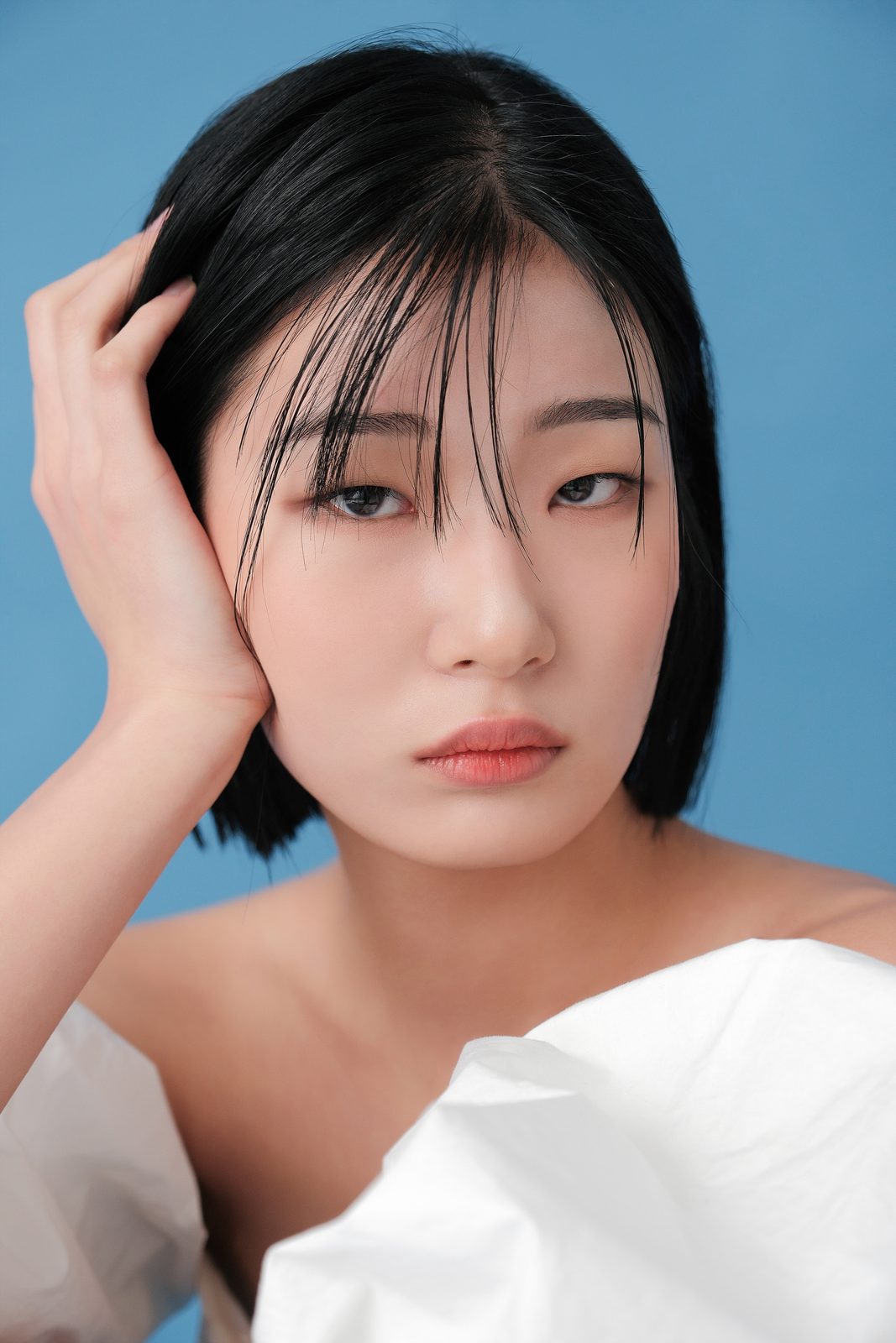 파란 배경에서 손으로 머리를 쓸어 올린 단발 여성 모델