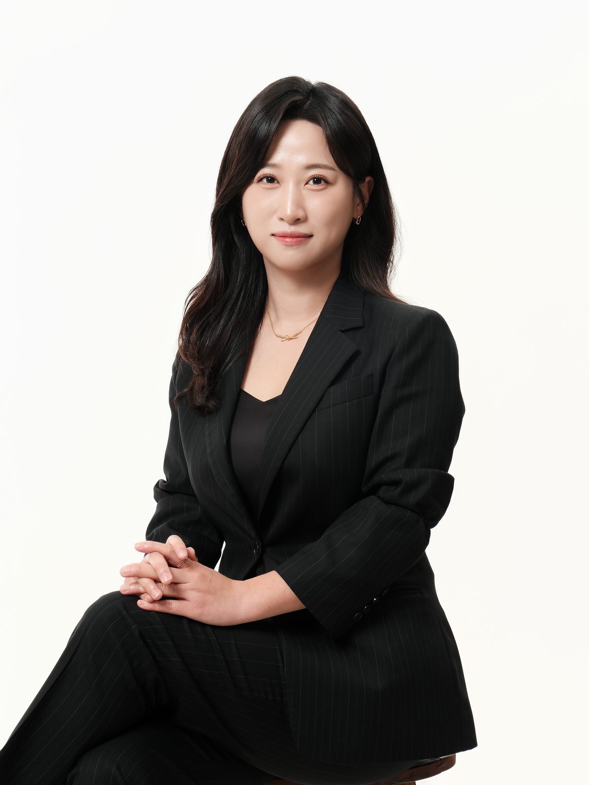 검은 정장을 입은 여성 직원이 의자에 앉아 손을 모은 프로필 사진